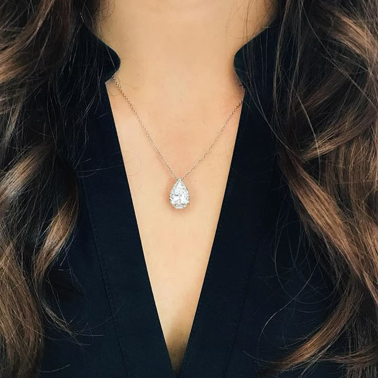 Teardrop-shaped diamond necklace worn by a person with long hair and a dark outfit.